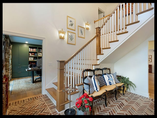 stairs featuring brick floor, a towering ceiling, and baseboards