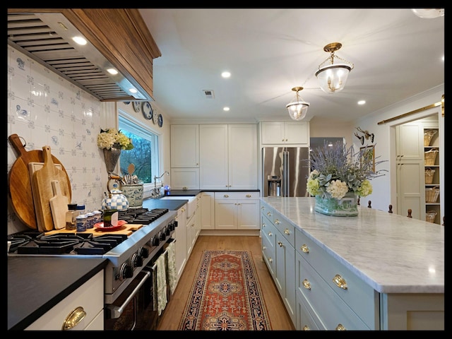 kitchen with visible vents, high end appliances, premium range hood, white cabinetry, and a sink