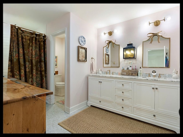 full bath with double vanity, a sink, toilet, and baseboards