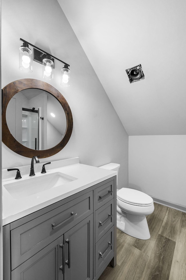 bathroom with hardwood / wood-style flooring, vanity, toilet, and vaulted ceiling