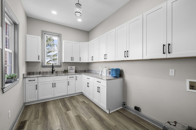 kitchen featuring wood-type flooring, sink, hanging light fixtures, and white cabinets