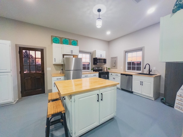 kitchen with sink, appliances with stainless steel finishes, white cabinetry, a kitchen breakfast bar, and decorative light fixtures