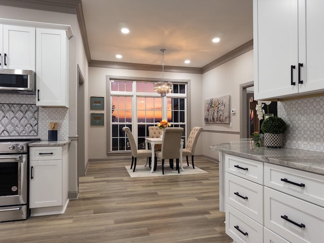 kitchen featuring crown molding, appliances with stainless steel finishes, hanging light fixtures, and white cabinets