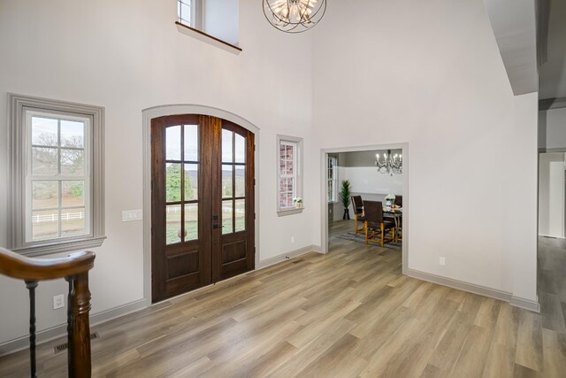 entryway featuring an inviting chandelier, light hardwood / wood-style floors, french doors, and a high ceiling