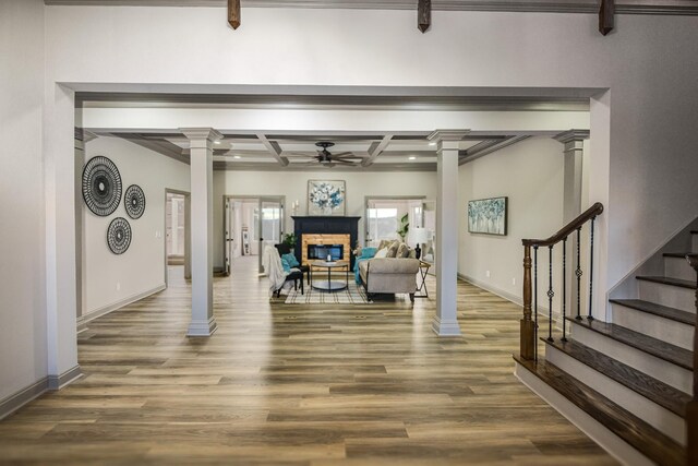 workout area featuring coffered ceiling, a stone fireplace, ornate columns, hardwood / wood-style flooring, and ceiling fan