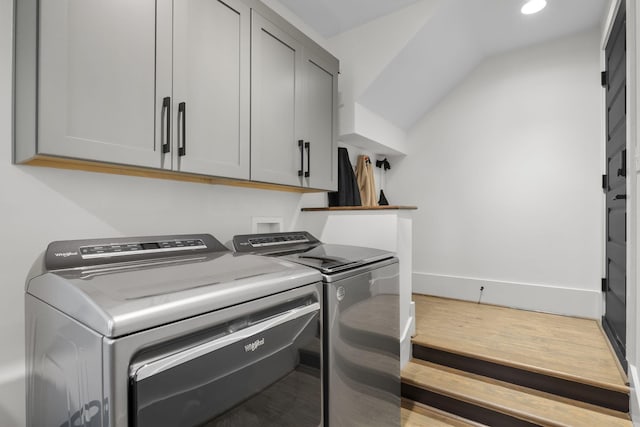 washroom featuring cabinets, washing machine and clothes dryer, and light hardwood / wood-style flooring