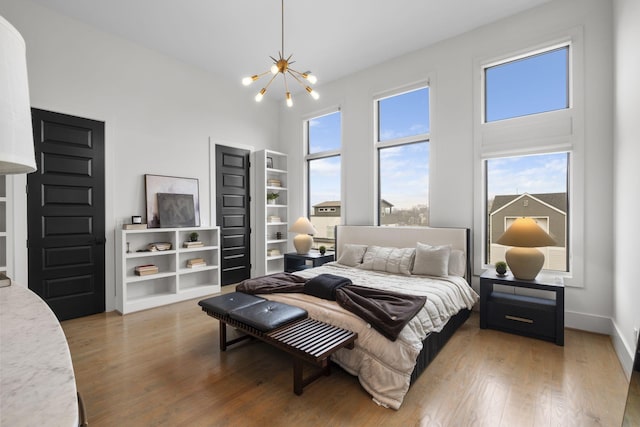 bedroom featuring a towering ceiling, wood-type flooring, and a notable chandelier