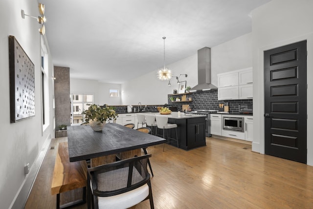 kitchen with appliances with stainless steel finishes, pendant lighting, white cabinetry, wall chimney range hood, and light wood-type flooring