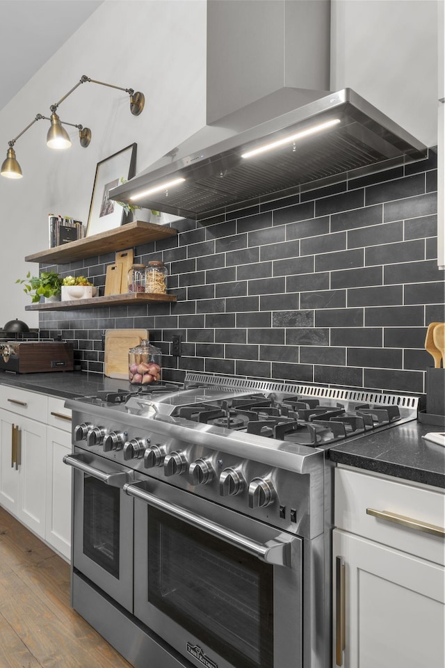 kitchen featuring hardwood / wood-style floors, white cabinets, decorative backsplash, range with two ovens, and wall chimney range hood