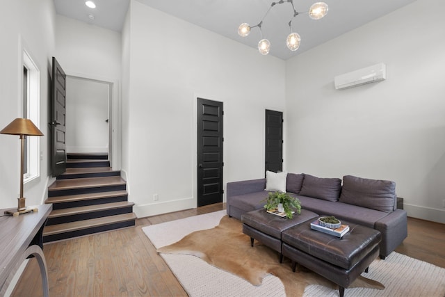 living room featuring a notable chandelier, a towering ceiling, hardwood / wood-style floors, and an AC wall unit