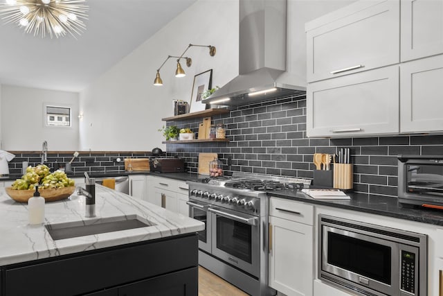 kitchen with sink, white cabinetry, dark stone counters, stainless steel appliances, and wall chimney range hood