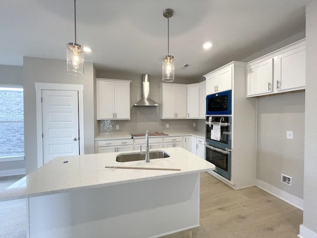 kitchen featuring a sink, white cabinets, built in microwave, wall chimney exhaust hood, and an island with sink