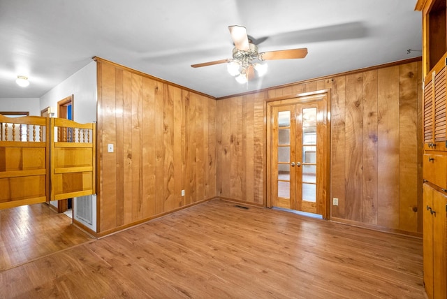 spare room with wood walls, light wood-type flooring, and french doors