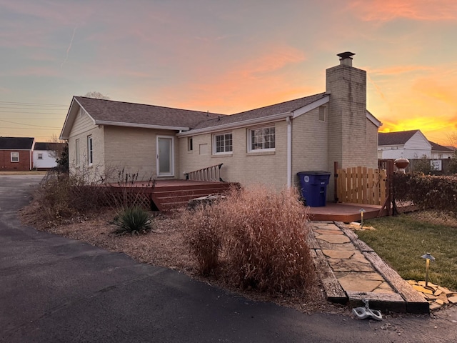 back of property at dusk with a chimney, fence, a deck, and brick siding