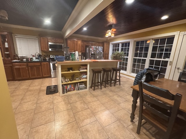 kitchen with light tile patterned floors, brown cabinetry, a ceiling fan, appliances with stainless steel finishes, and ornamental molding