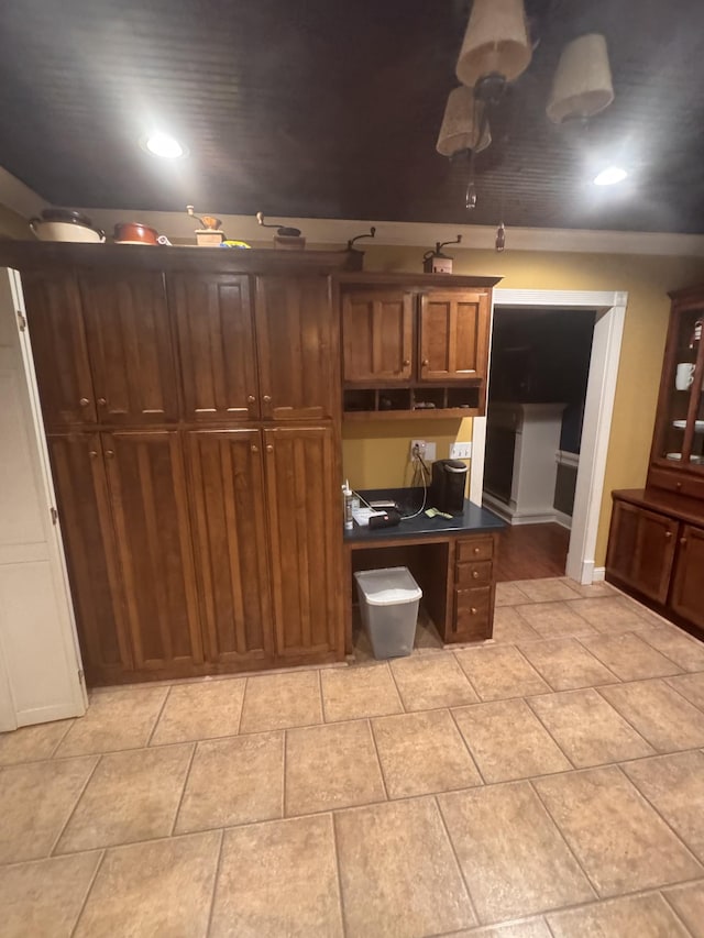 kitchen featuring light tile patterned floors, dark countertops, brown cabinets, built in desk, and recessed lighting