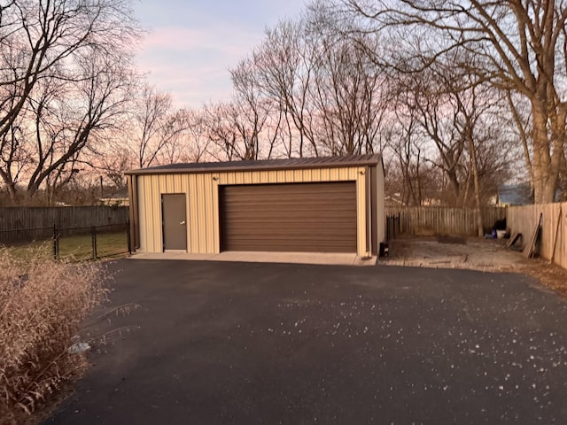 garage at dusk featuring a detached garage and fence