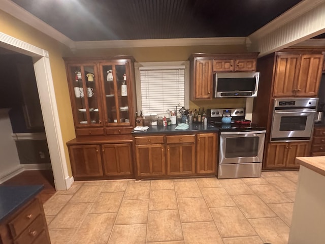 kitchen featuring stainless steel appliances, ornamental molding, brown cabinetry, and glass insert cabinets