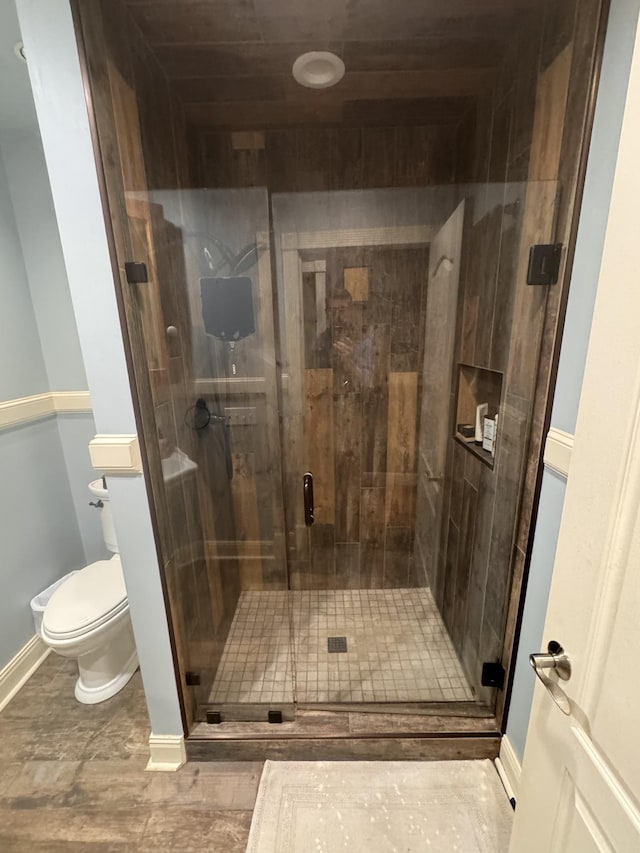 bathroom with toilet, a stall shower, and baseboards