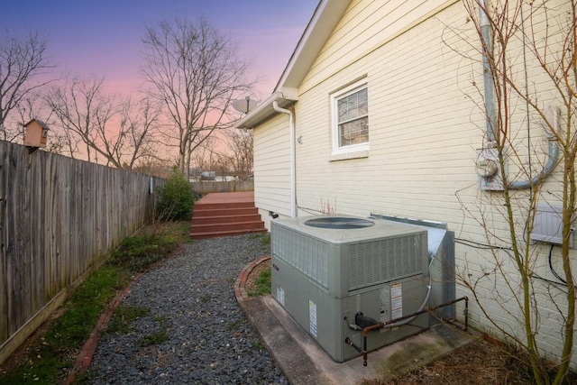 view of property exterior featuring brick siding, fence, and central air condition unit