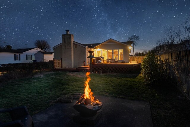 rear view of property featuring an outdoor fire pit, a fenced backyard, a yard, a wooden deck, and a chimney