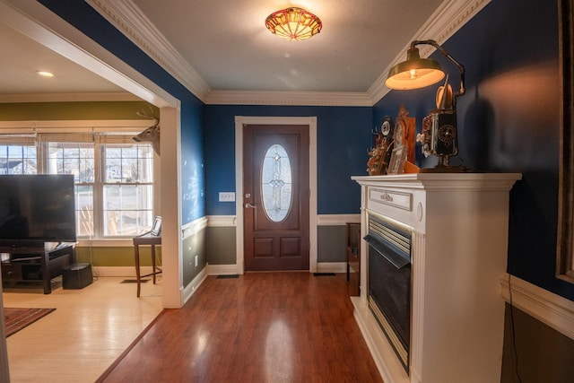 entrance foyer featuring ornamental molding, a wainscoted wall, a fireplace, and wood finished floors