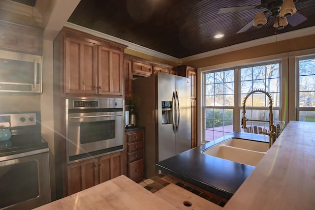 kitchen with a sink, appliances with stainless steel finishes, brown cabinets, plenty of natural light, and crown molding