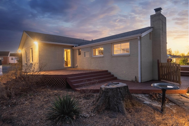 back of property at dusk featuring a wooden deck, a chimney, and brick siding