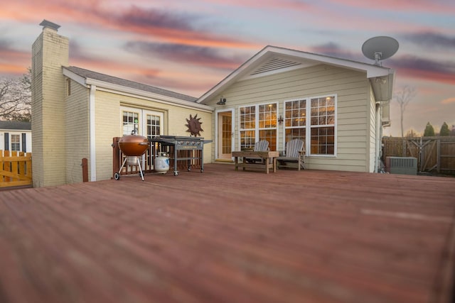 back of house at dusk featuring fence, a chimney, a wooden deck, and central air condition unit