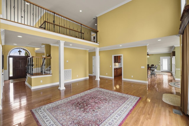 living room with ceiling fan, a high ceiling, wood-type flooring, ornamental molding, and ornate columns