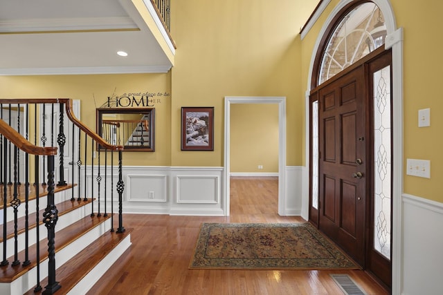 foyer with crown molding, wood-type flooring, and a towering ceiling