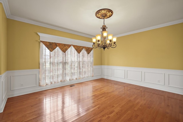 empty room featuring wood-type flooring, ornamental molding, and a chandelier