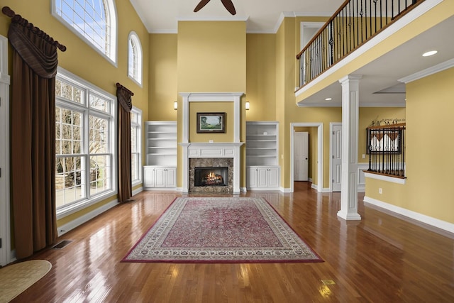 unfurnished living room with crown molding, wood-type flooring, a premium fireplace, and ornate columns