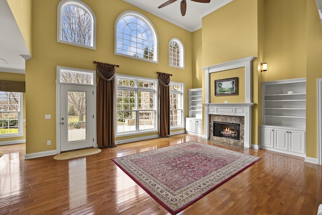 living room featuring crown molding, hardwood / wood-style flooring, ceiling fan, a towering ceiling, and a fireplace