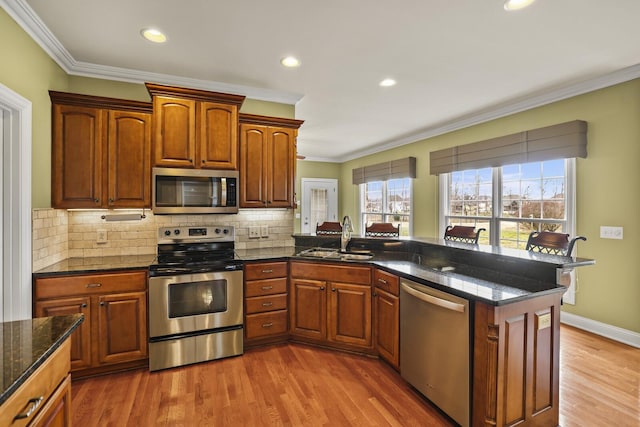 kitchen with stainless steel appliances, crown molding, sink, and dark stone countertops