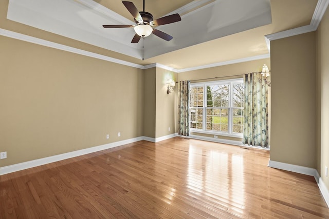 empty room featuring crown molding, ceiling fan, a tray ceiling, and light wood-type flooring