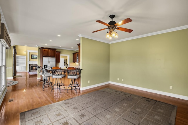 kitchen with a kitchen bar, wood-type flooring, ornamental molding, stainless steel fridge, and kitchen peninsula