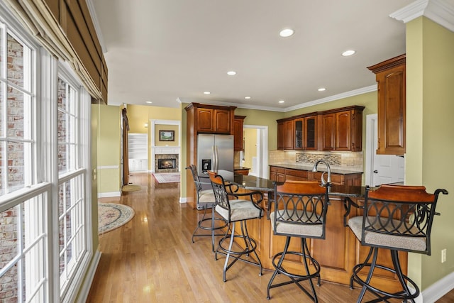 kitchen with tasteful backsplash, ornamental molding, a kitchen bar, and stainless steel fridge with ice dispenser