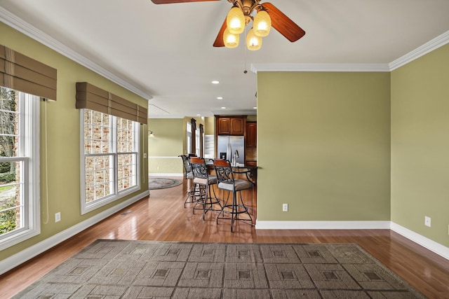 kitchen featuring crown molding, wood-type flooring, stainless steel fridge with ice dispenser, and a breakfast bar area