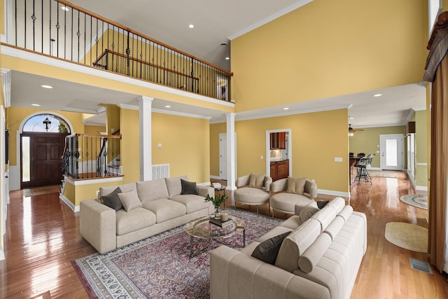 living room featuring crown molding, light hardwood / wood-style flooring, ceiling fan, a towering ceiling, and ornate columns