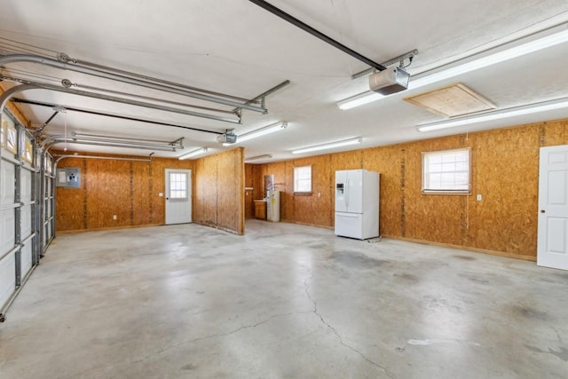 garage with a garage door opener, white refrigerator with ice dispenser, and electric panel