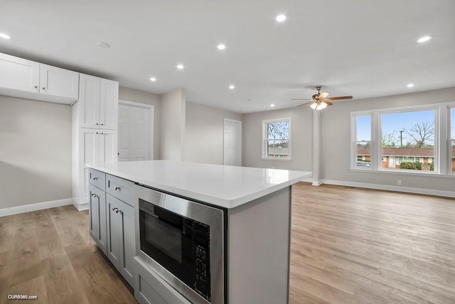 kitchen featuring light hardwood / wood-style flooring, white cabinetry, gray cabinetry, a center island, and stainless steel microwave