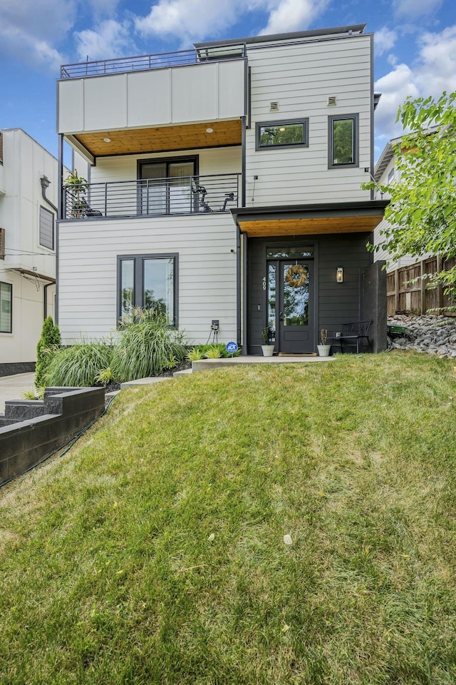 rear view of property featuring a balcony and a yard