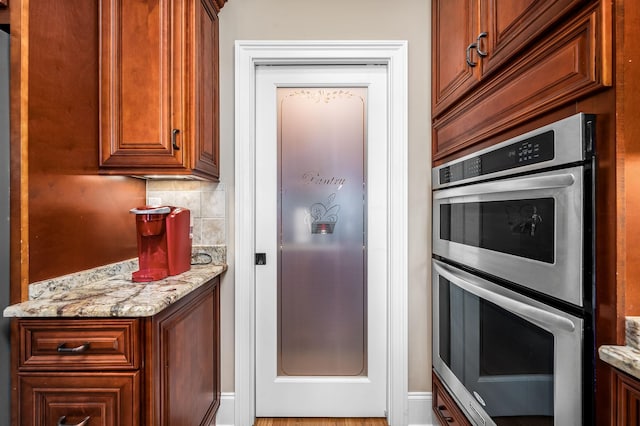 kitchen featuring light stone counters, decorative backsplash, and stainless steel double oven