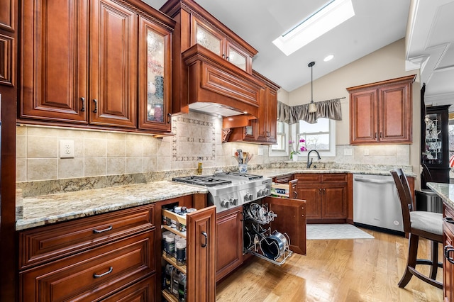 kitchen with lofted ceiling with skylight, pendant lighting, light hardwood / wood-style floors, stainless steel appliances, and light stone countertops