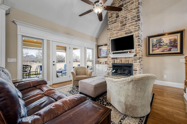 living room with wood-type flooring, a stone fireplace, ceiling fan, and high vaulted ceiling