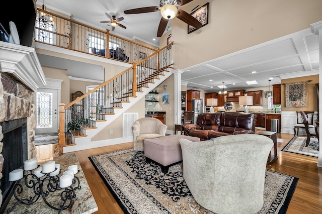 living room featuring a high ceiling, ornamental molding, a stone fireplace, and dark wood-type flooring