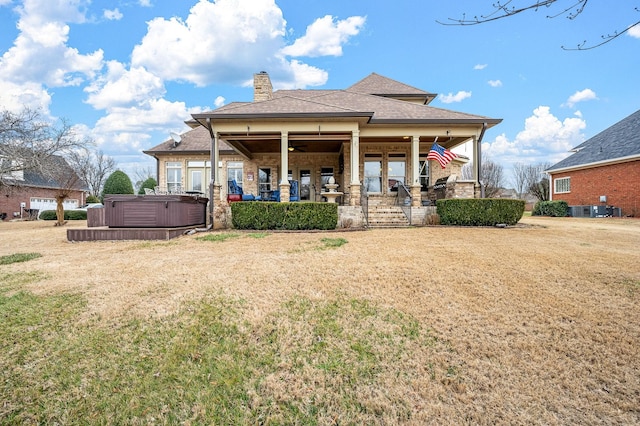 rear view of property with a hot tub, central AC, covered porch, and a lawn