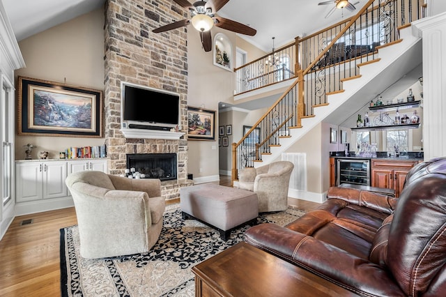 living room featuring a stone fireplace, wet bar, ceiling fan, beverage cooler, and light hardwood / wood-style floors