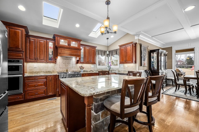 kitchen with lofted ceiling with skylight, decorative light fixtures, a center island, stainless steel appliances, and light hardwood / wood-style floors